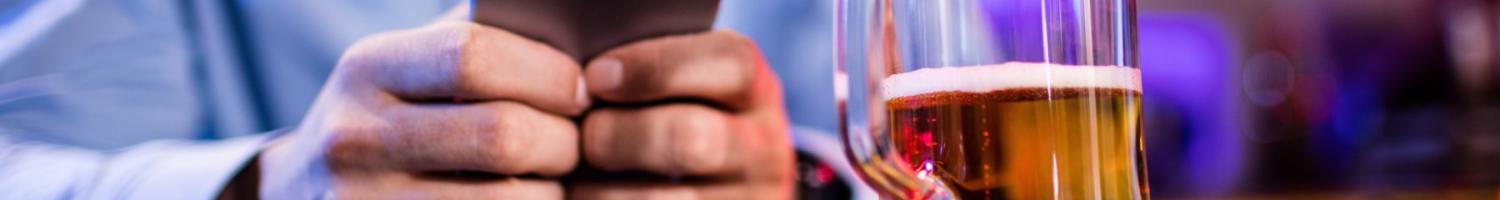 Photo of a man using a cellphone with a beer glass in foreground 