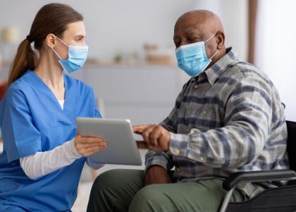Photo of elderly Black patient using healthcare provider's tablet computer