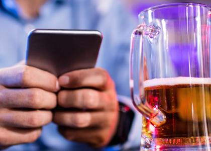 Photo of a man using a cellphone with a beer glass in foreground 