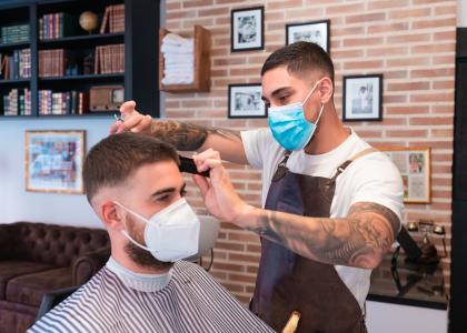 Photo of man receiving haircut from barber, both wearing masks