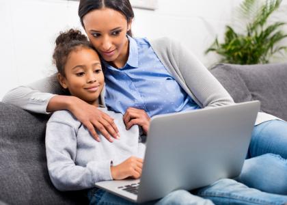 Photo of child and mother on couch using laptop