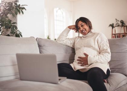 Photo of pregnant Black woman using laptop on couch