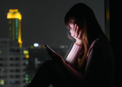 Photo of depressed woman using cellphone at night by window