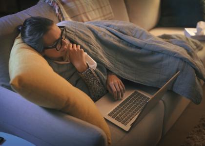 Photo of a sick woman on a couch using a laptop